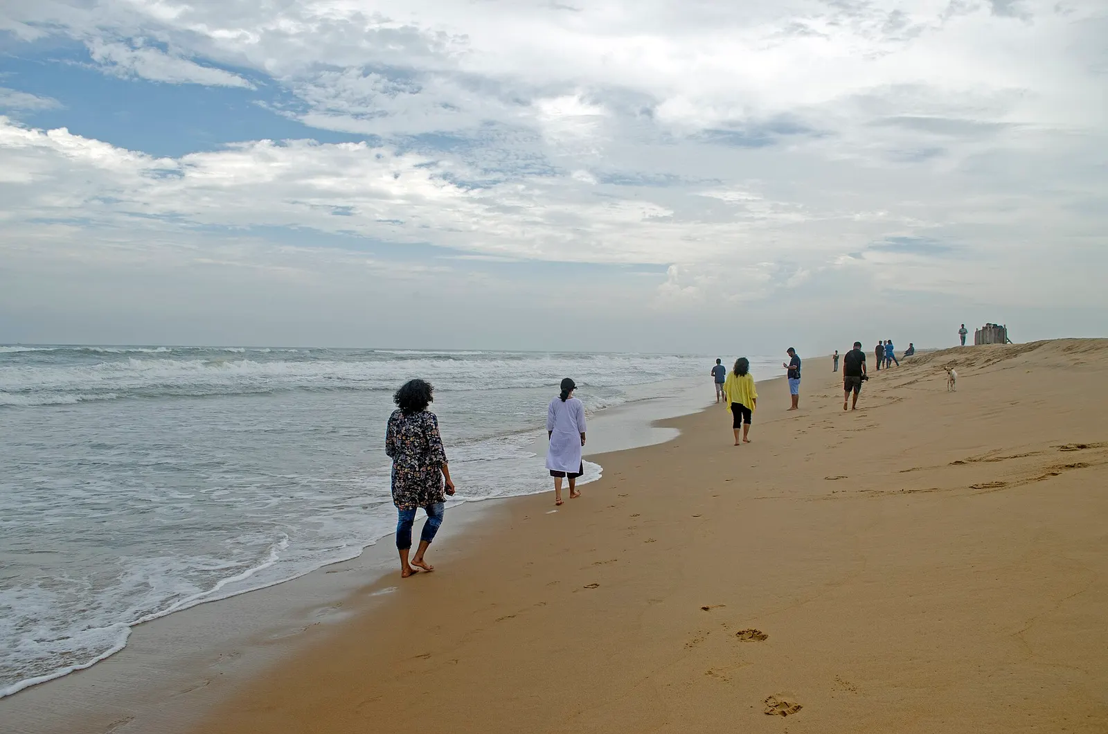 Visitors walking on the sandbar at the Chilika sea mouth with surf breaking on the Bay of Bengal side