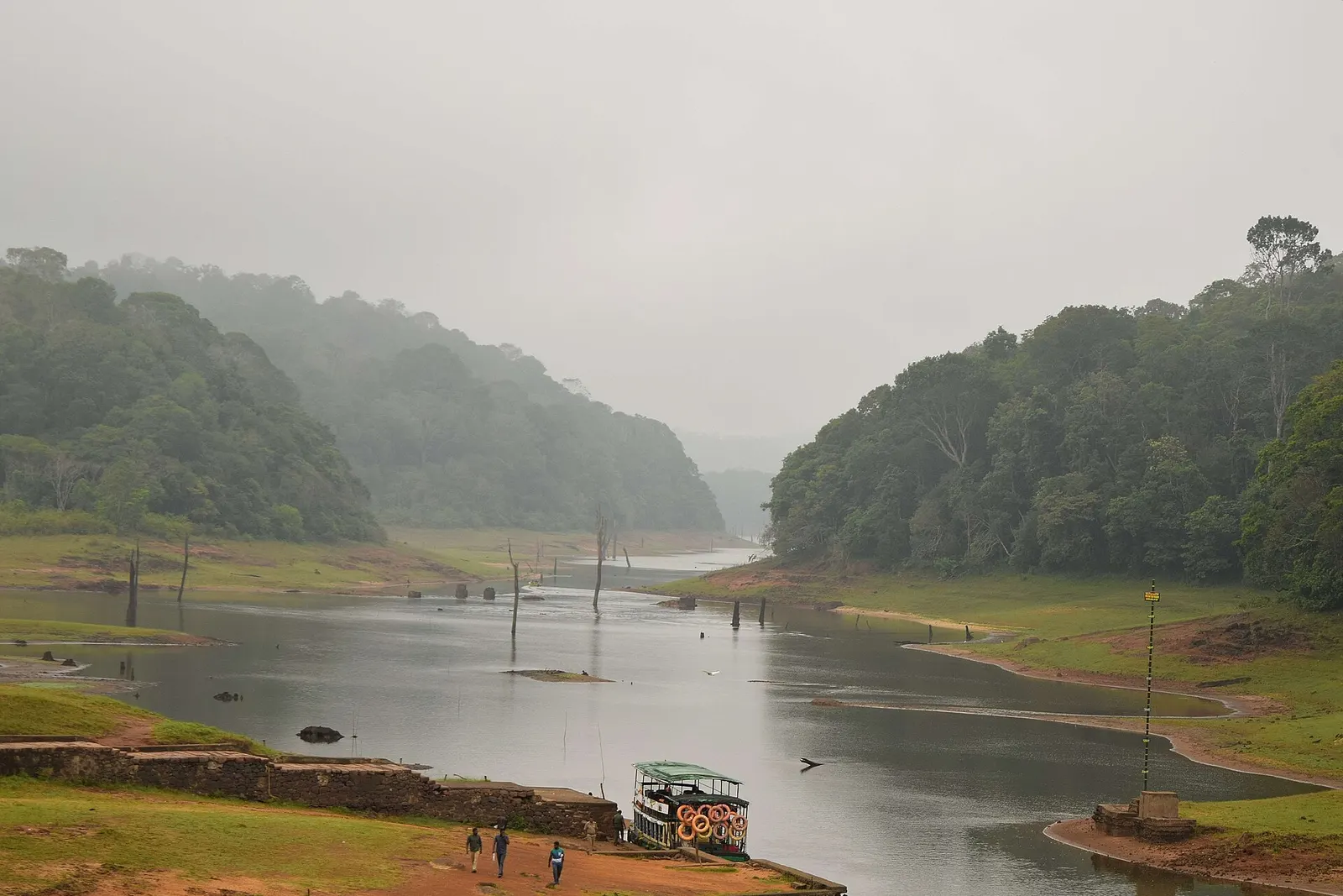 The boat landing on Periyar lake at Thekkady, with dead tree stumps in the shallow water below forested hills