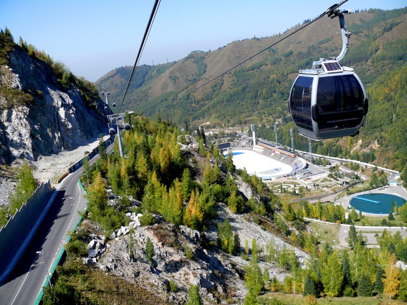 A gondola cabin on the cable car above the Medeu rink and the road up the gorge, photographed in early autumn before the snow arrives